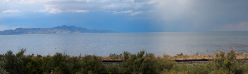 [Three photos stitched together (with photo edge demarcations somewhat visible) showing greenery at the foreground, the lake in the mid-ground and mountains in the distance off to the left.]